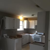 Kitchen mid-repaint with freshly painted white cabinets