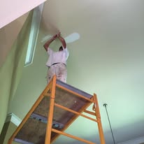 Painter on a ladder finishing a vaulted ceiling around a ceiling fan