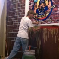 Artist painting a large colorful custom mural on a brick wall
