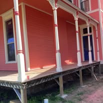 Detail of the finished Victorian house's red porch columns and blue front door